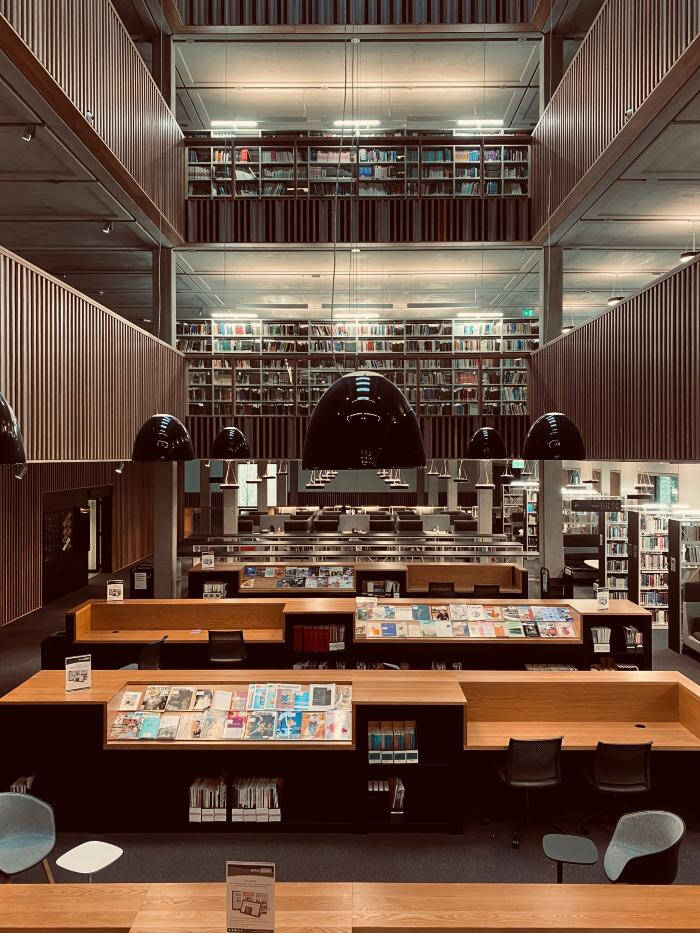 Colored photograph of the inside of a mutli-story library. Tables at the lower level, stacks of books visible on the upper floors.
